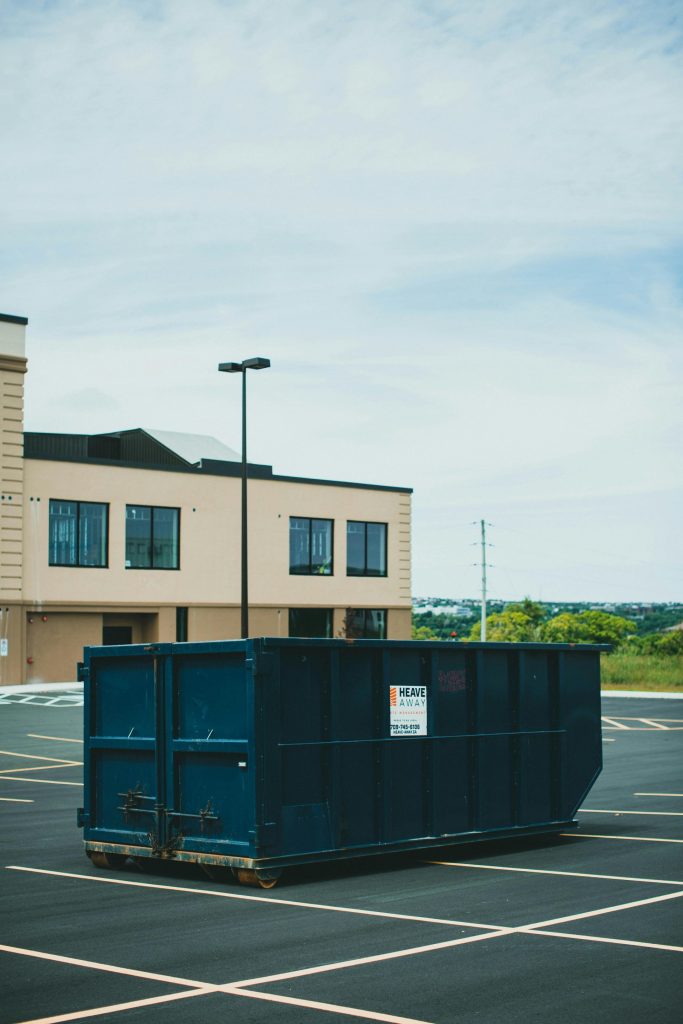 Blue industrial dumpster placed in an empty parking lot outside a commercial building.